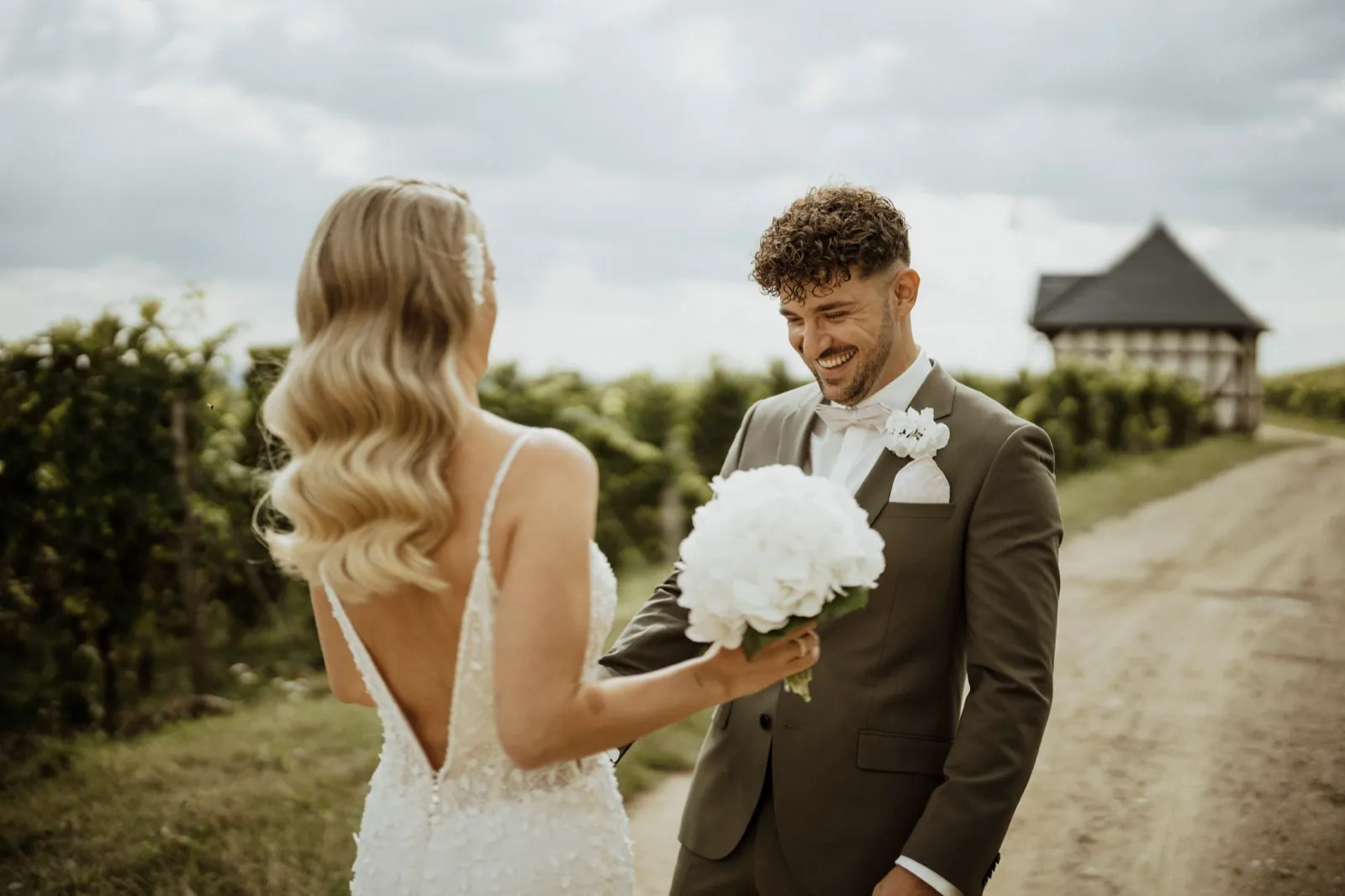 Luisa & Norman – Ein Bräutigam lächelt, während die Braut ihm ihren Brautstrauß zeigt