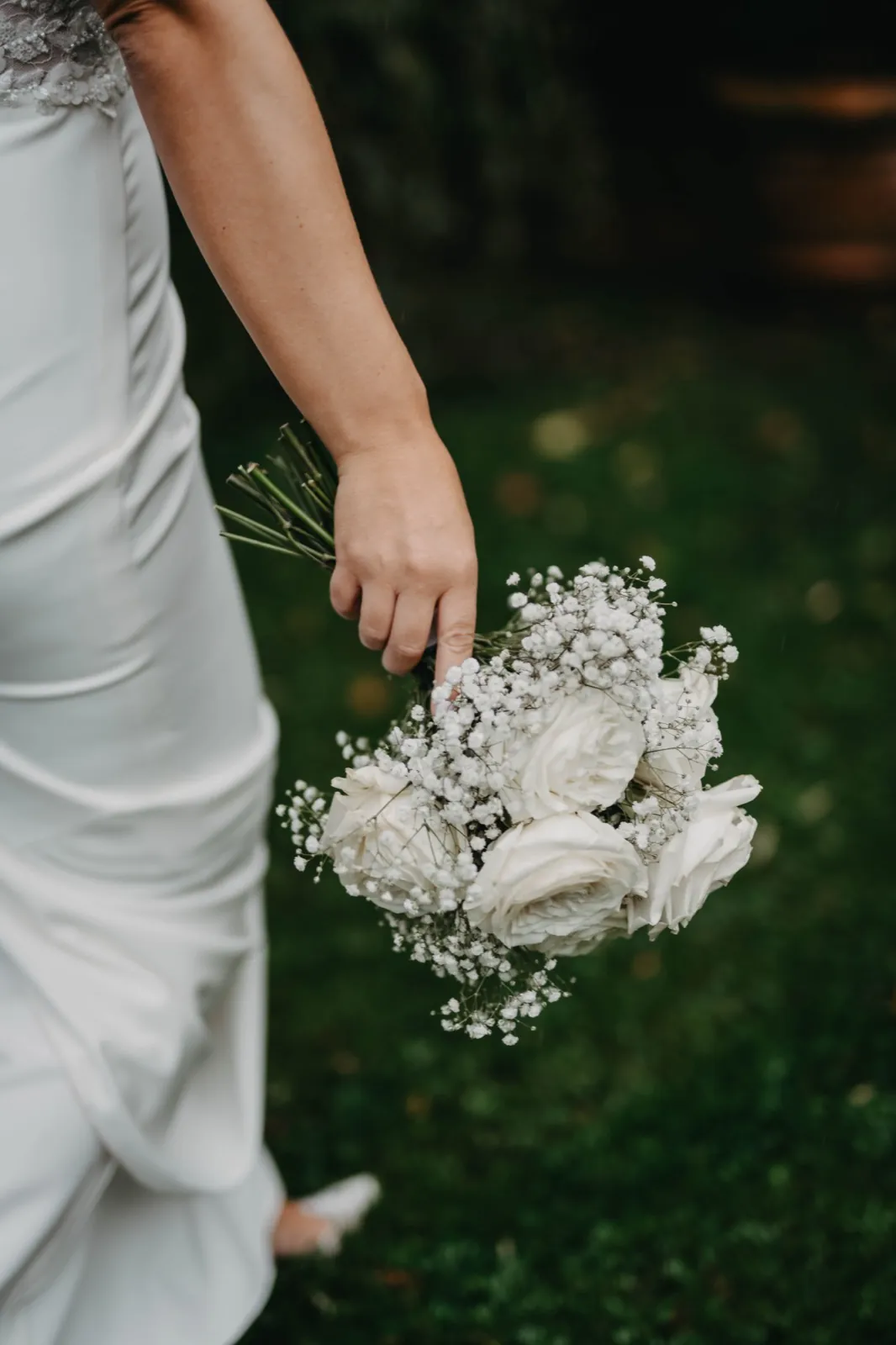Alina & Timo – Eine Braut hält ihren weißen Brautstrauß aus Rosen und Schleierkraut in der Hand