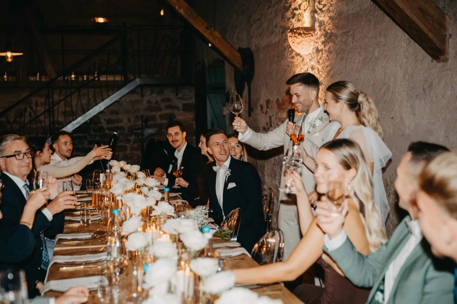 Alina & Timo – Ein Bräutigam hält eine Rede an einer festlich geschmückten Tafel während einer Hochzeitsfeier