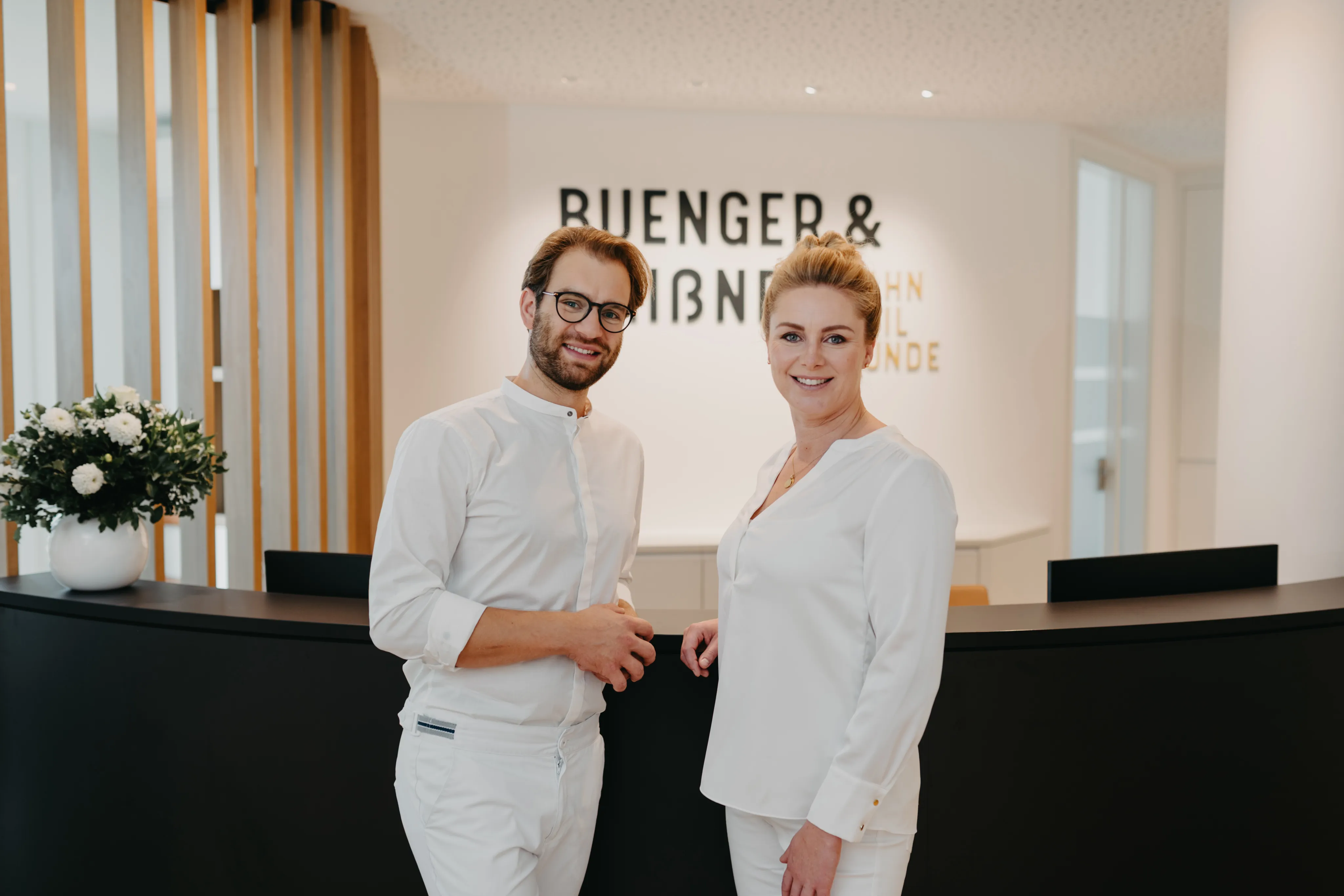 Bünger & Meißner – Ein Mann und eine Frau in weißer Arbeitskleidung stehen lächelnd an einer Rezeption