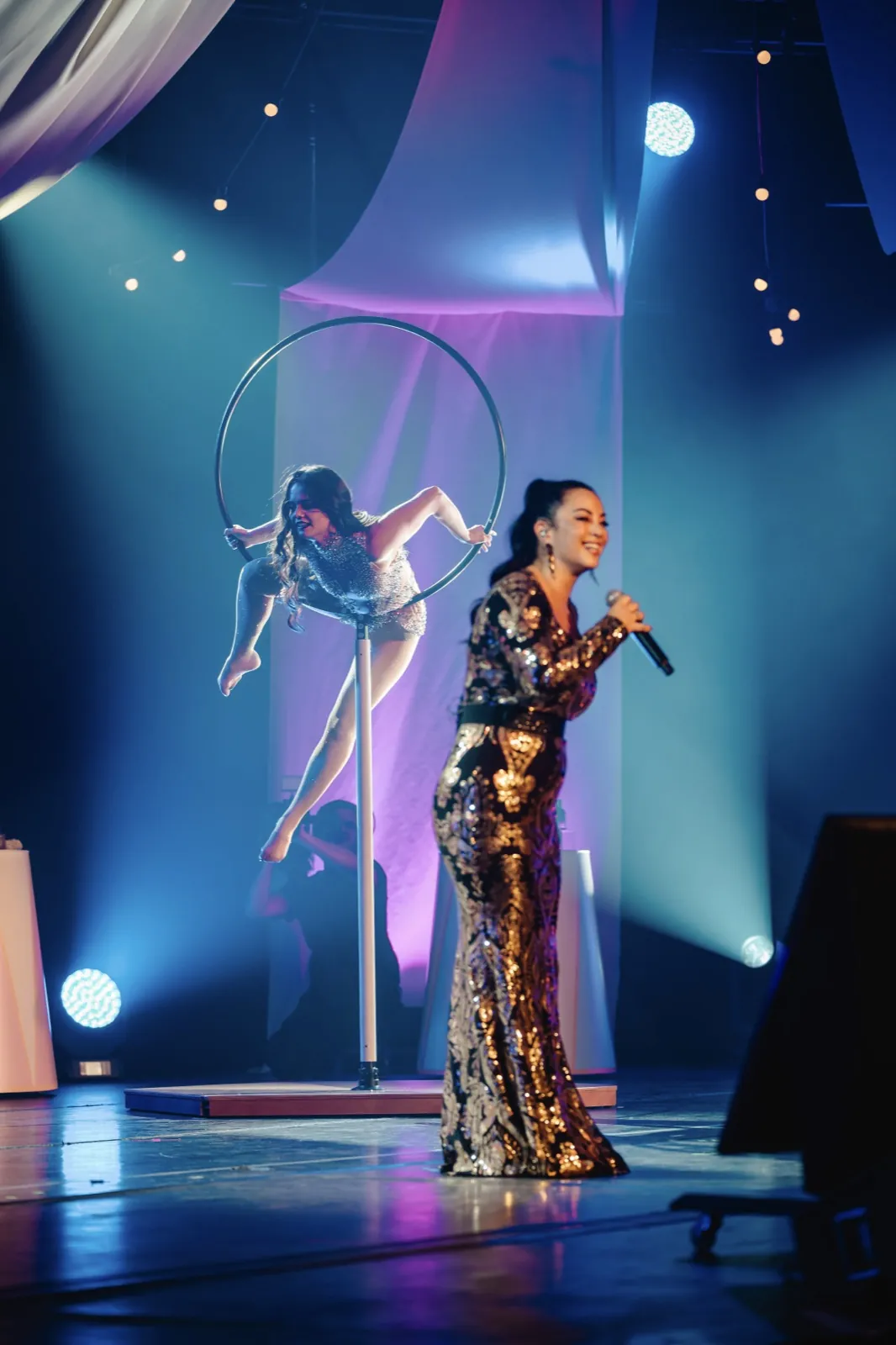 Cirque Inspiré – Eine Sängerin tritt auf einer Bühne auf, während im Hintergrund eine Akrobatin turnt