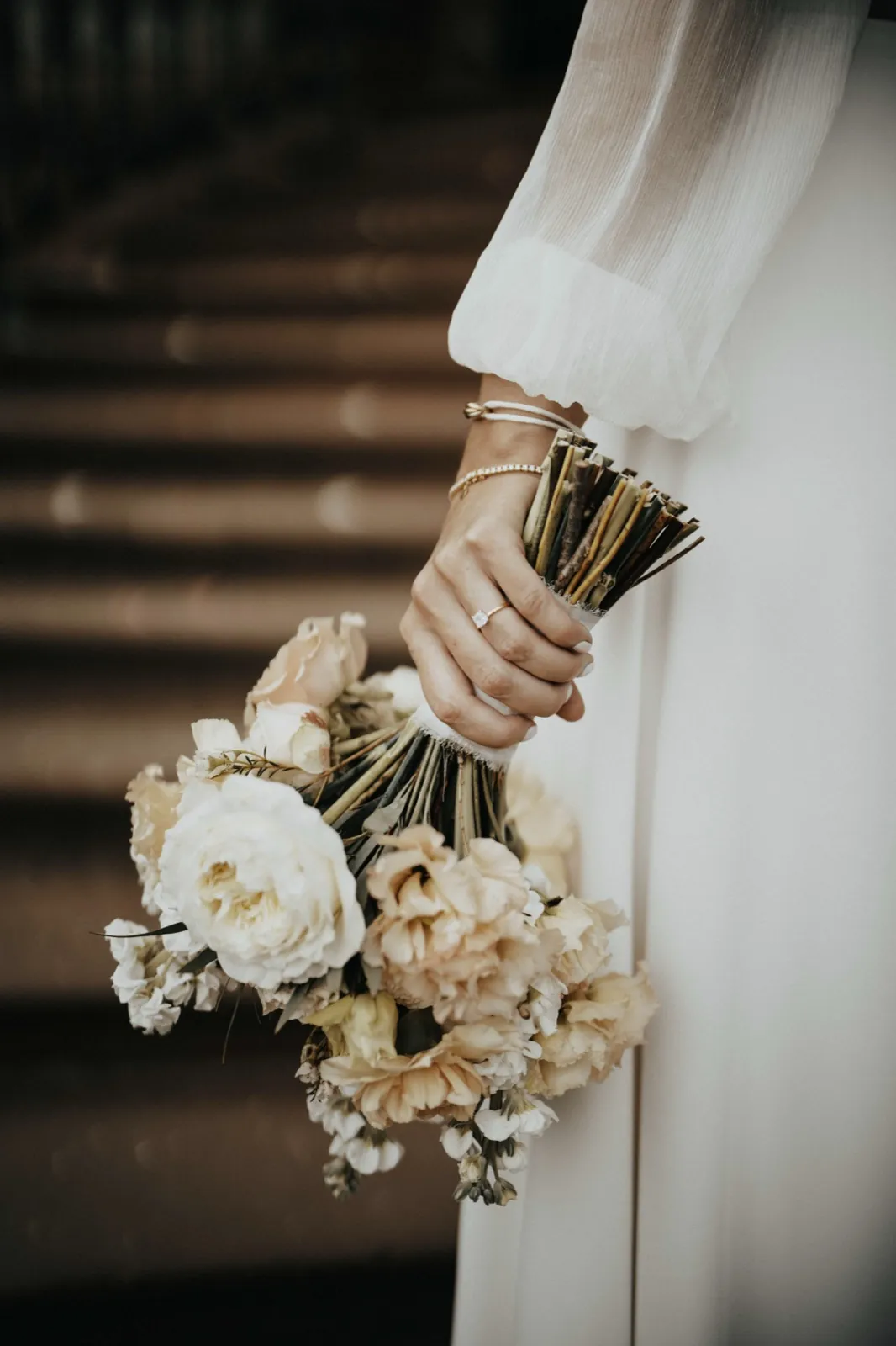 Deana & Sebastian – Eine Braut hält ihren eleganten Brautstrauß mit hellen Blumen in der Hand