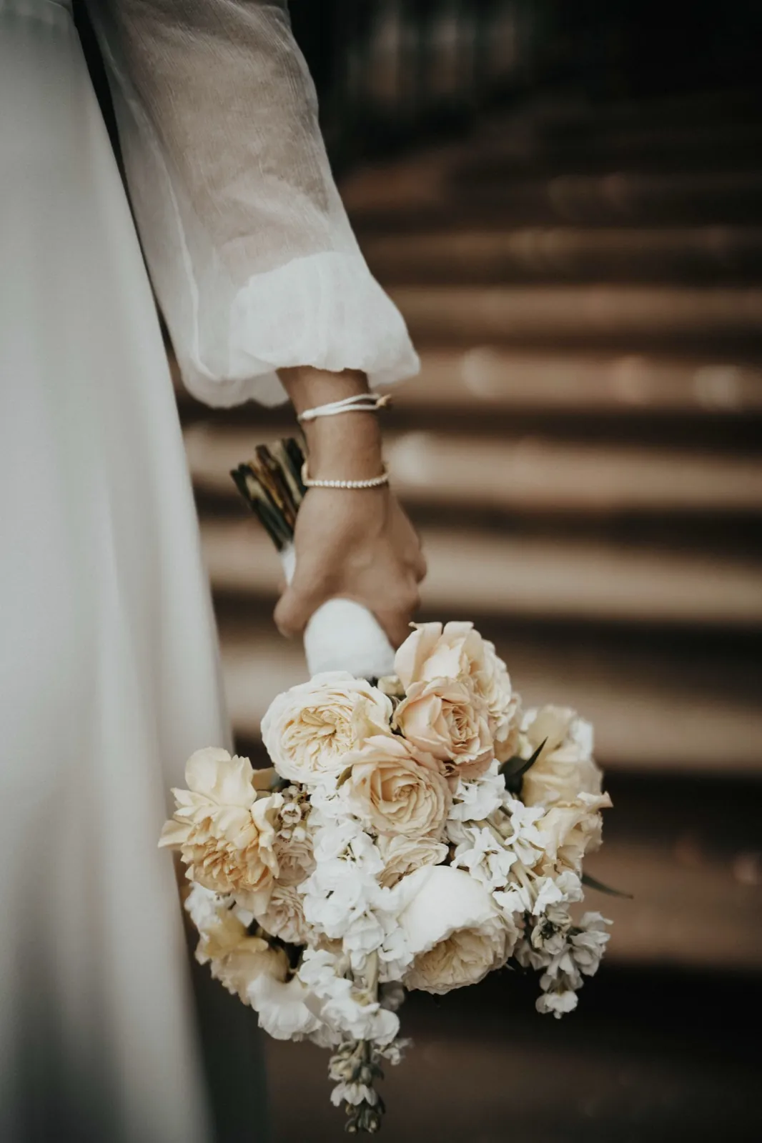Deana & Sebastian – Eine Braut hält ihren eleganten Brautstrauß aus cremefarbenen Rosen und weißen Blüten