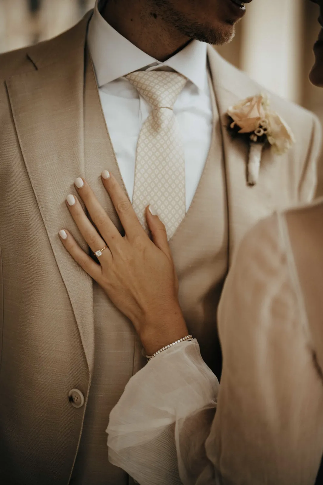 Deana & Sebastian – Eine Detailaufnahme der Hand einer Braut mit Ring auf der Brust des Bräutigams