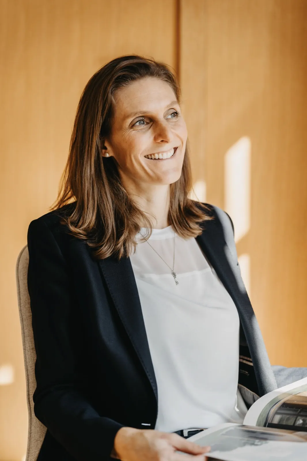 Franziska Hildenbrandt – Eine lächelnde Frau im Business-Outfit sitzt vor einer Holzwand und hält ein Buch