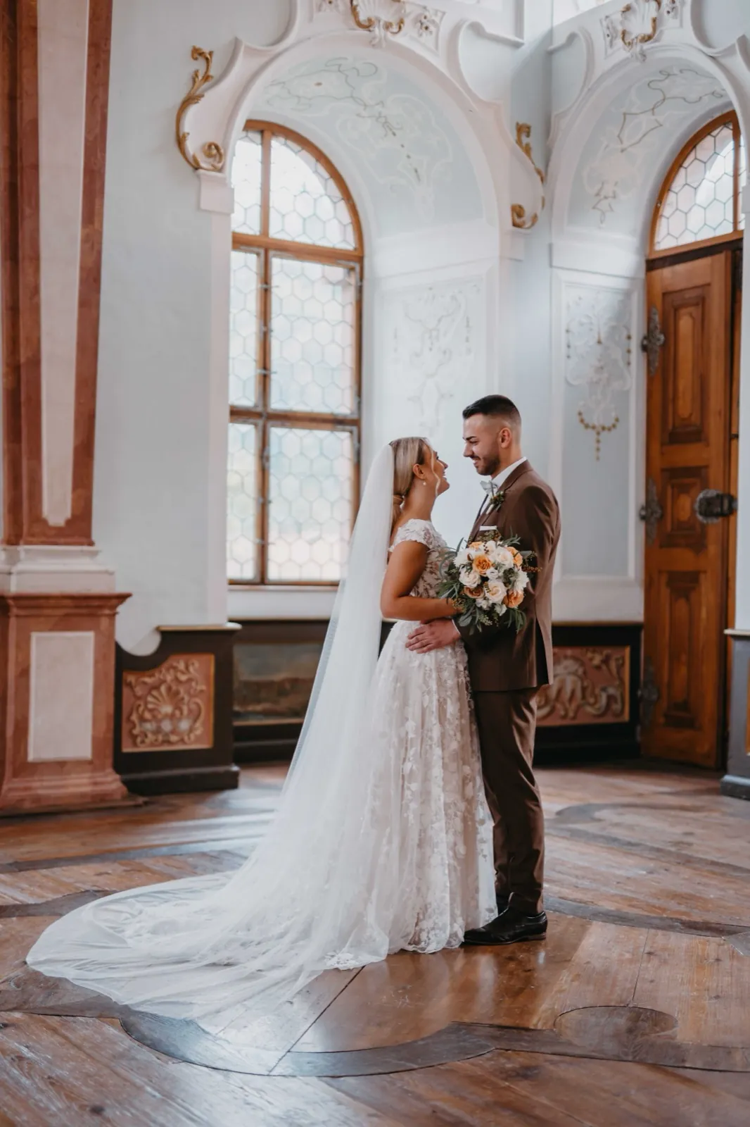 Jana & Daniel – Ein Brautpaar steht sich in einem prunkvollen Saal gegenüber und schaut sich lächelnd an