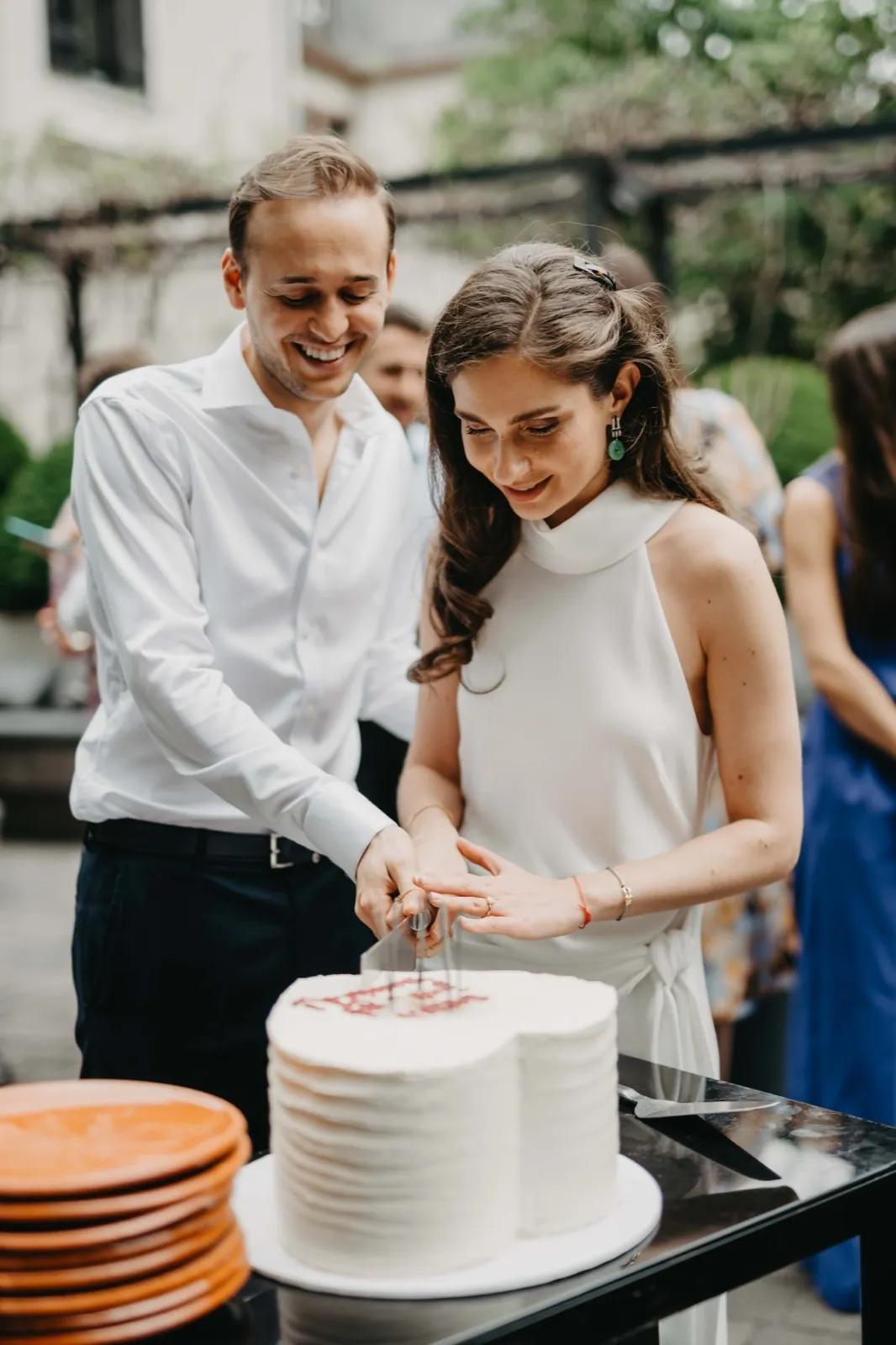 Jessica & Adrian – Ein Brautpaar schneidet gemeinsam eine weiße Hochzeitstorte an und lächelt dabei