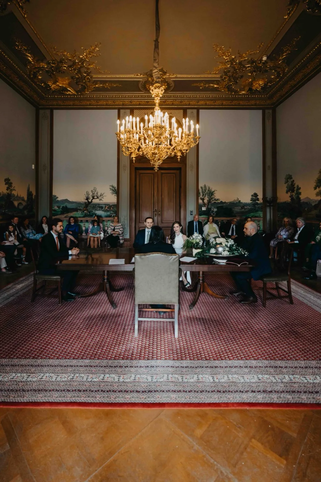 Jessica & Adrian – Eine Hochzeitszeremonie in einem prunkvollen Saal mit Gästen im Hintergrund