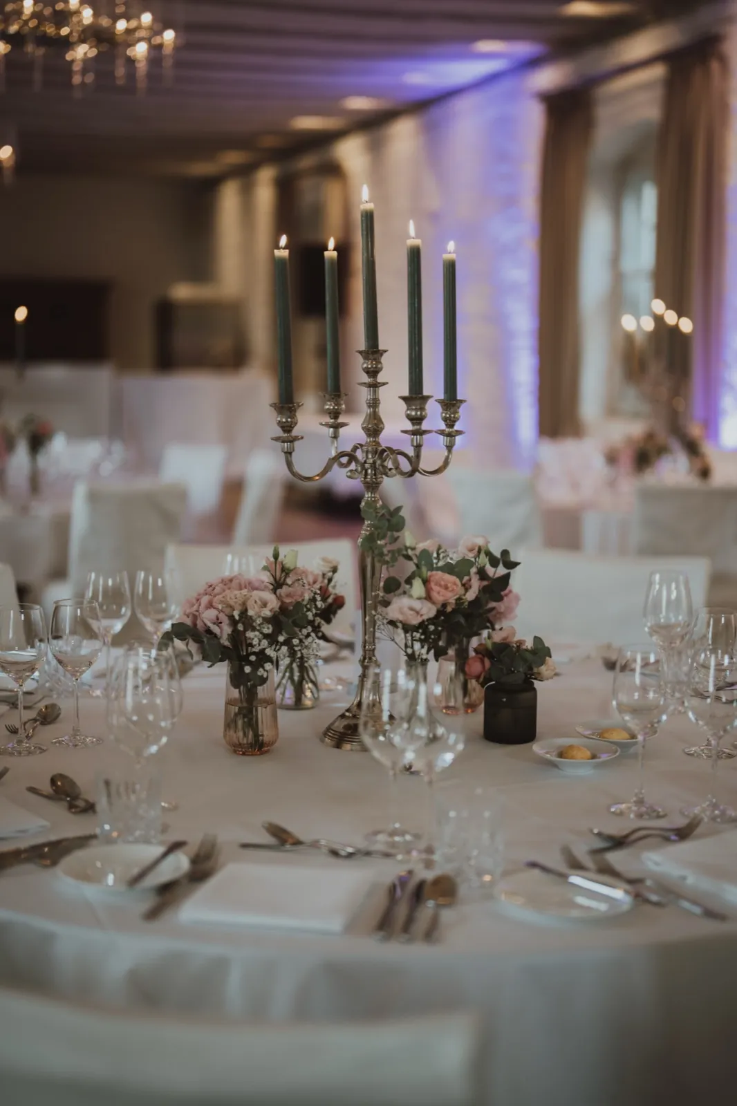 Julia & Chris – Ein festlich gedeckter Tisch mit einem silbernen Kerzenständer und zarten Blumenarrangements