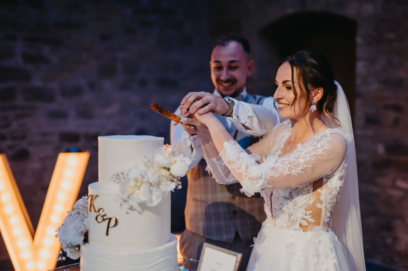 Kristina & Pascal – Ein Brautpaar schneidet gemeinsam die weiße Hochzeitstorte an