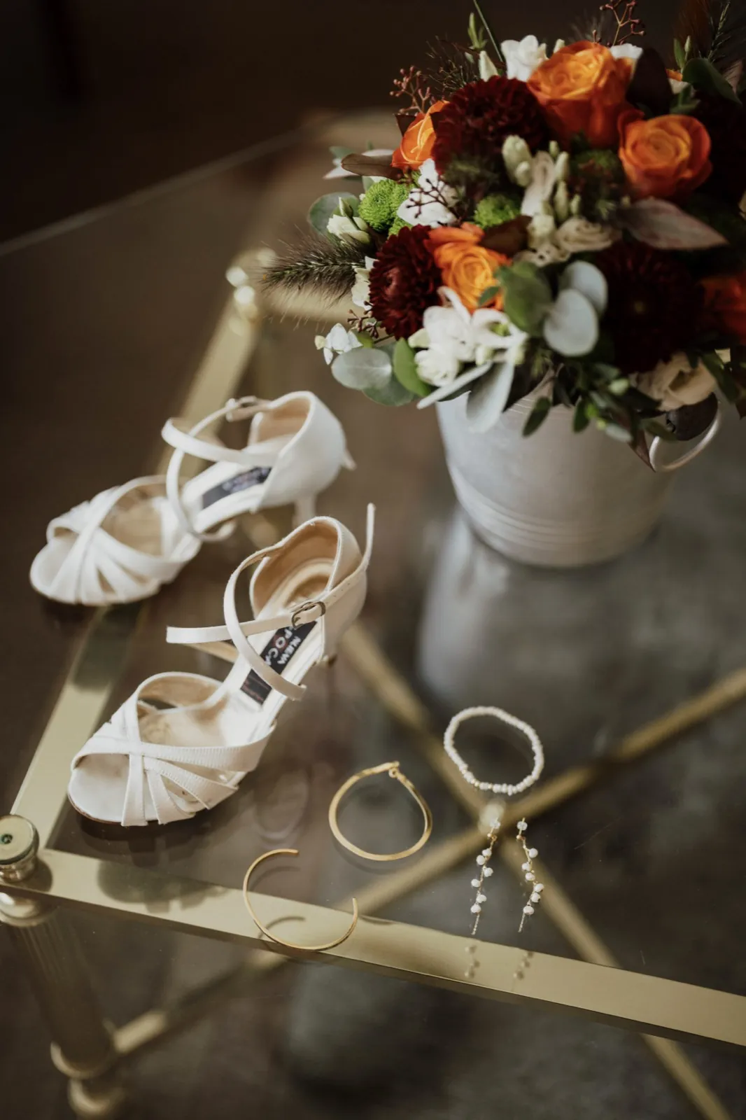 Marie & Thomas – Brautschuhe, Schmuck und ein herbstlicher Blumenstrauß liegen auf einem Glastisch