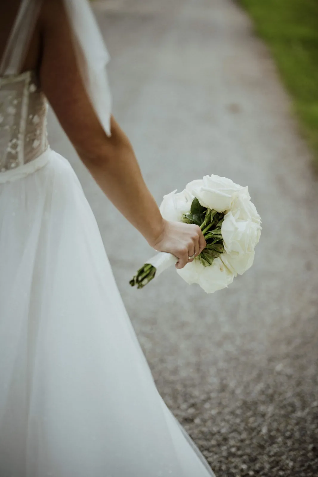 Nadine & Raphael – Eine Braut von hinten fotografiert hält einen Strauß weißer Rosen in der Hand