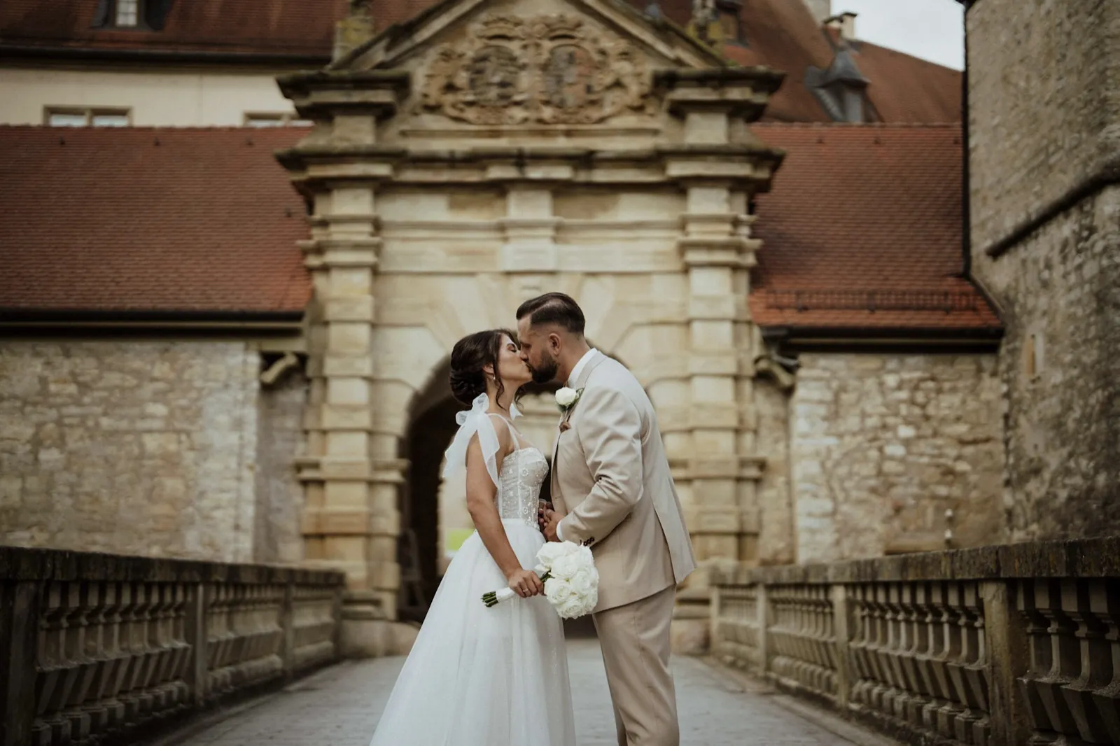 Nadine & Raphael – Ein Brautpaar küsst sich auf einer Brücke vor einem historischen Schlosstor