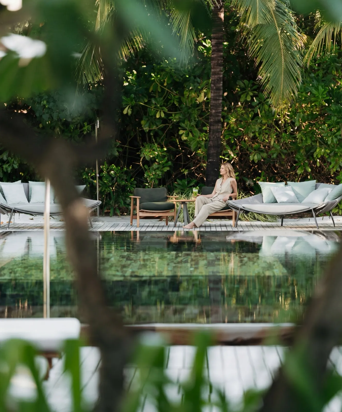 Patina Maldives – Eine Frau entspannt auf einer Liege am Pool eines tropischen Resorts