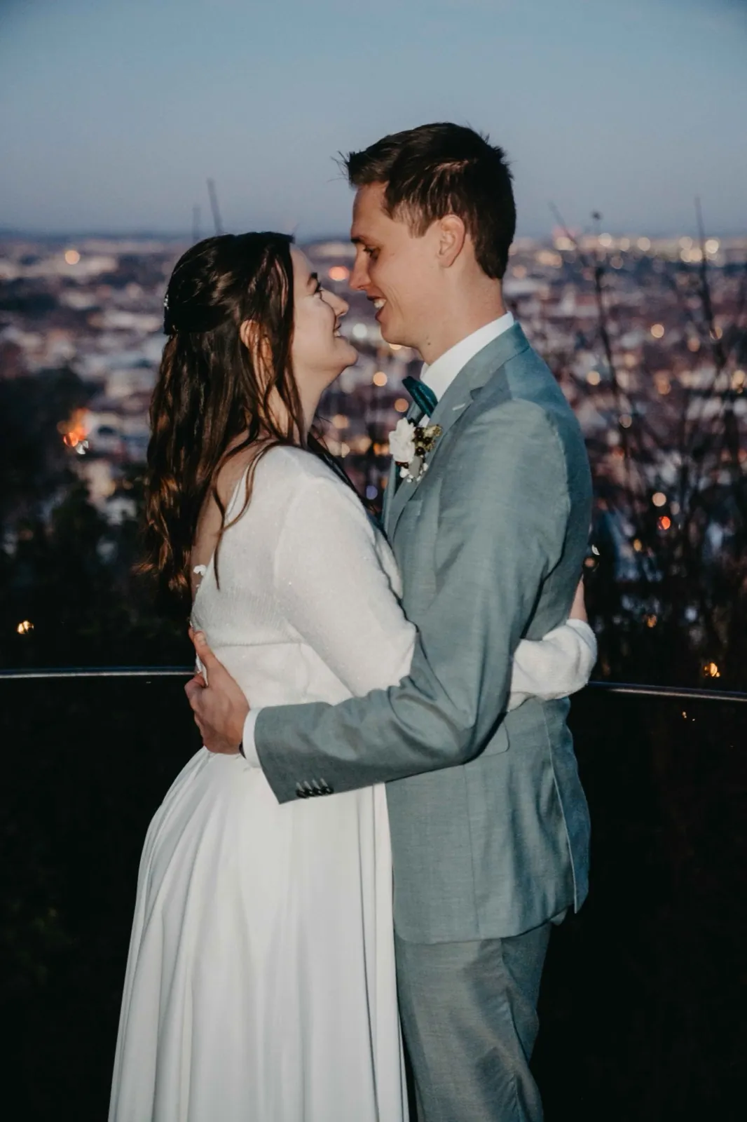 Sophie & Mirko – Abendliche Umarmung vor beleuchteter Stadtkulisse