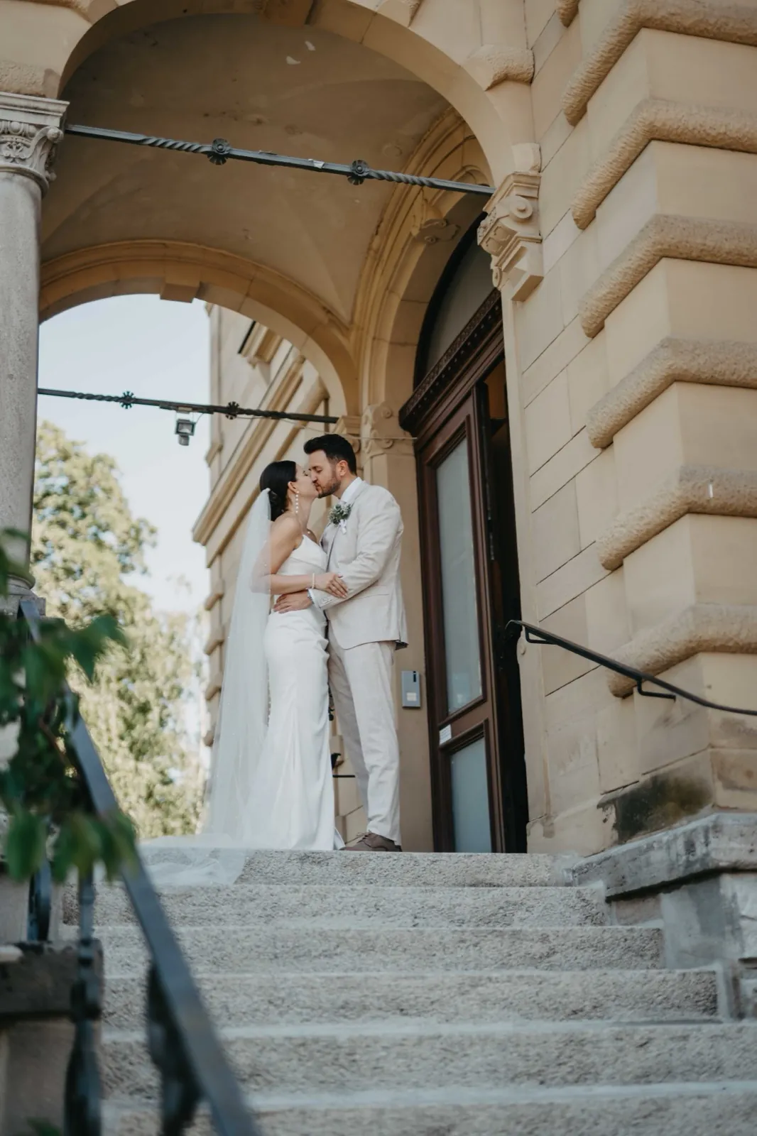 Verena & Rafael – Ein Brautpaar küsst sich auf den Stufen vor einem historischen Gebäude