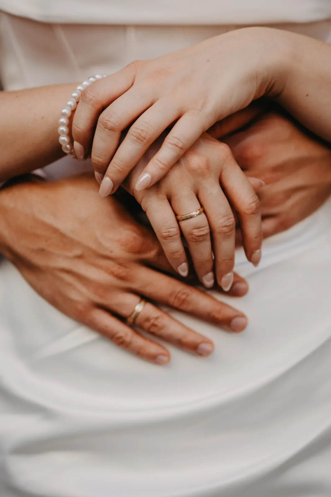 Verena & Rafael – Nahaufnahme von ineinandergelegten Händen eines Brautpaares mit Eheringen und einem Perlenarmband