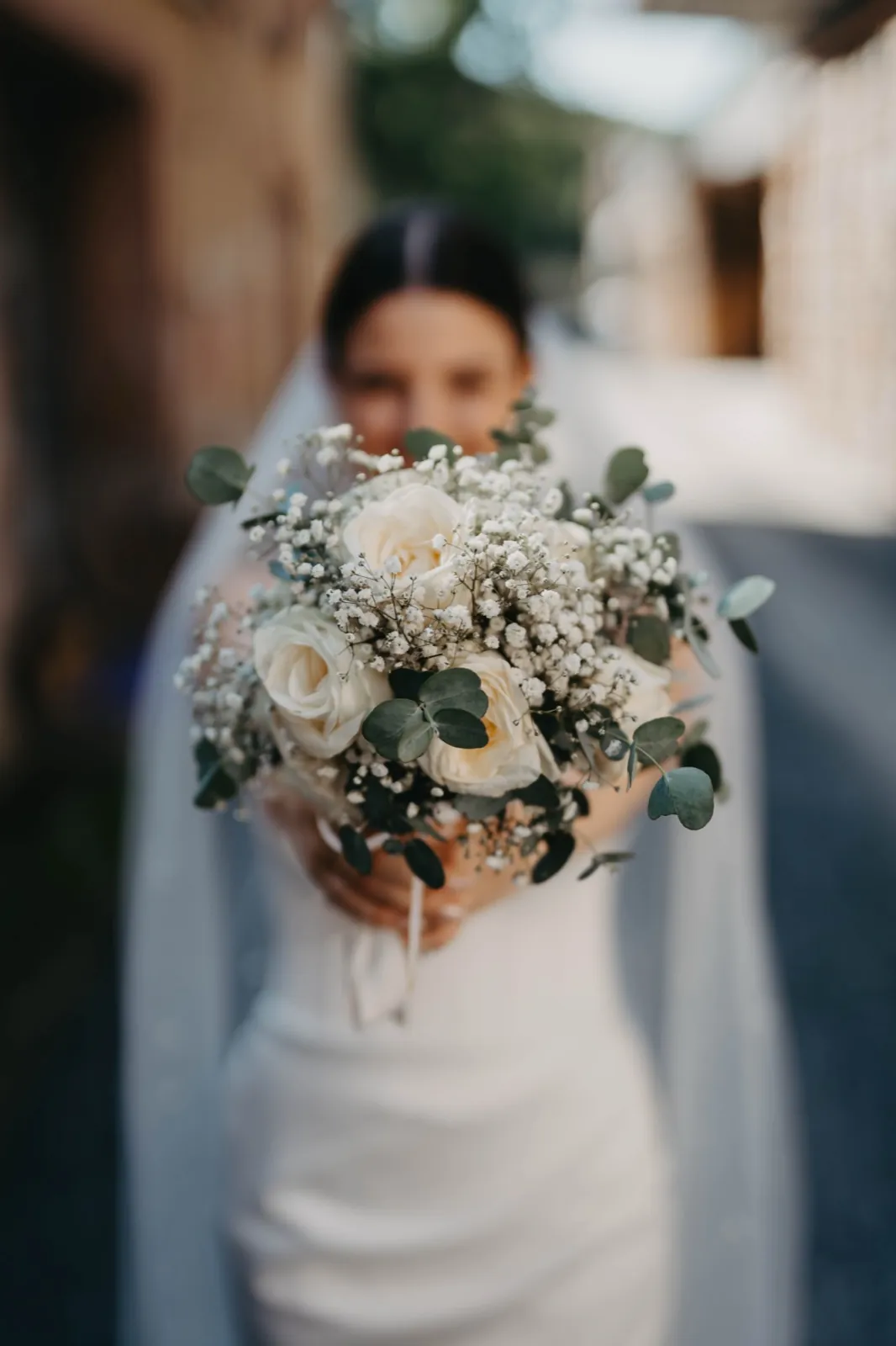 Verena & Rafael – Eine Braut hält ihren Brautstrauß mit weißen Rosen und Schleierkraut in die Kamera